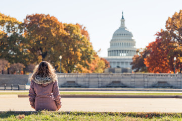 Young woman in coat sitting looking at view of United States Congress Capitol building, golden...