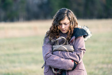 Young sad woman girl walking with eyes closed down holding hugging purse in winter coat, unhappy stomach ache pain