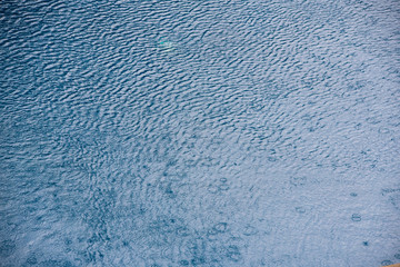 Water with small waves and raindrops on a pool with blue texture background
