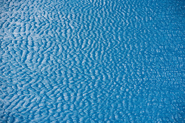 Water with small waves and raindrops on a pool with blue texture background