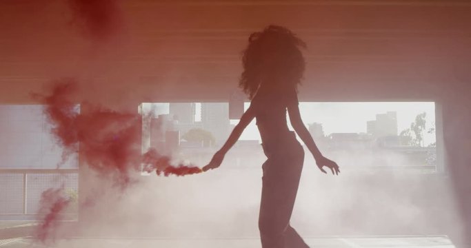 Silhouette young woman dancing with colorful red smoke bomb in parking garage