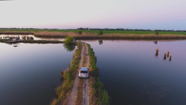 Aerial photography. The car moves along a narrow road between the lakes. Fish pond. Summer morning. Ivanovskaya. Krasnodar. Russia.