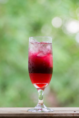 Mulberry juice in glass on wooden table against green background
