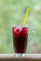 Mulberry juice in glass on wooden table against green background