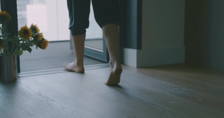 Young barefoot woman in sportswear walking to balcony