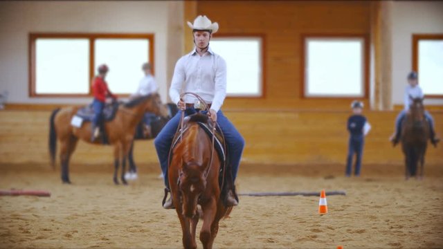 Young western rider focused on riding a pattern in slow motion 4K. Long shot of a male person on a horse in focus wearing a white shirt and cowboy hat riding towards the camera. 