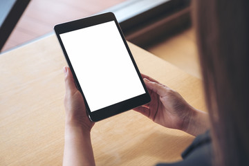 Mockup image of a woman holding and using a black tablet pc with blank white desktop screen on the table