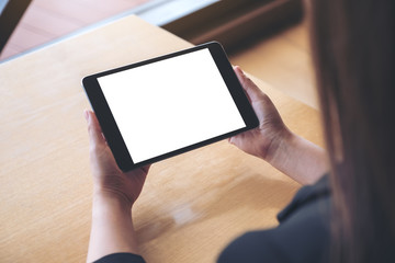 Mockup image of a woman holding and using a black tablet pc with blank white desktop screen on the table