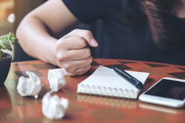Closeup image of a businesswoman upset and screwed up papers on table with notebook and mobile phone