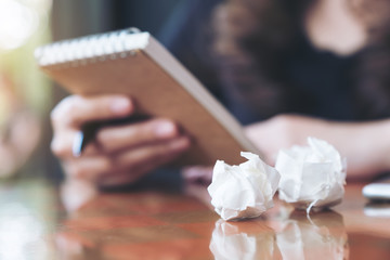 Obraz premium Closeup image of a businesswoman working and holding a white blank notebook with screwed up papers on table