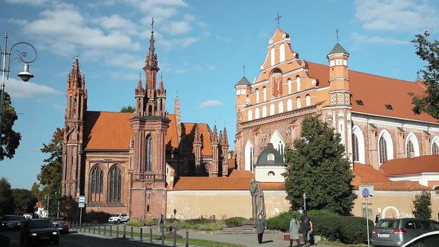 Vilnius, Lithuania. People Walking Near Roman Catholic Church Of St. Anne And Church Of St. Francis And St. Bernard In Old Town In Summer Sunny Day.