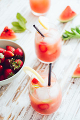 Watermelon and strawberries fruit juice on glass with mint leaves on a white board, flare from backlight.
