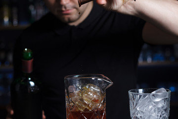 Bartender is pouring alcohol from a jigger into a measuring glass.