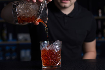 Barman pours alcohol or juice into a glass over ice.