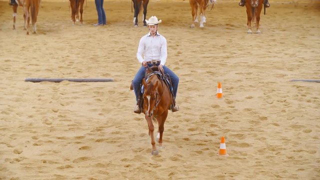 Western riding championship slow motion 4K. Long shot top view of a young cowboy in focus maneuvering around riding arena.