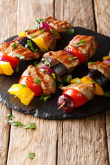 skewers of pork with tomatoes, pepper, onions and eggplants close-up on a slate plate on a table. vertical