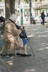 An elderly woman with a cane sits on a bench in the park