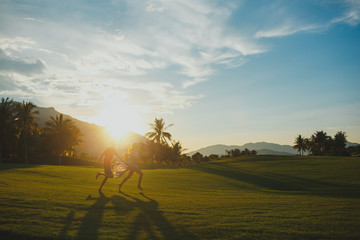 Obraz na płótnie Canvas happy loving couple running through the golf course on a beautiful sunrise of the sun