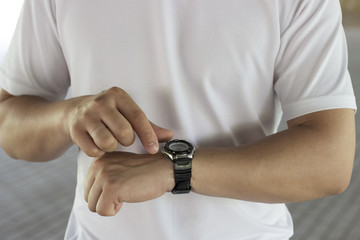 A man adjusts his watch on his arm against the background of a white T-shirt. The concept of time, time management
