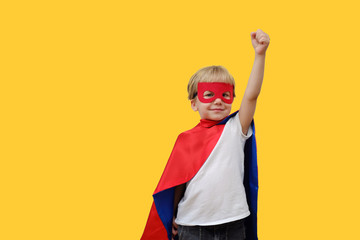 Cute boy in superhero costume on yellow background