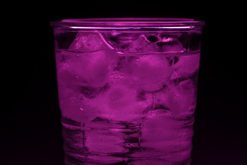 Glass with ice cubes in purple on a black background