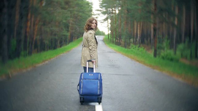 Young beautiful woman hitchhiking standing on the road with a suitcase on a table with an inscription SEA