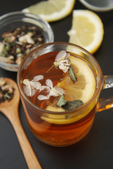 Glass Cup of Herbal Tea with Acacia Flowers, lemon, honey on Black Background, top view, Copy space. Health Drink Coldness
