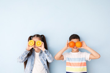 Funny little children with citrus fruit on color background