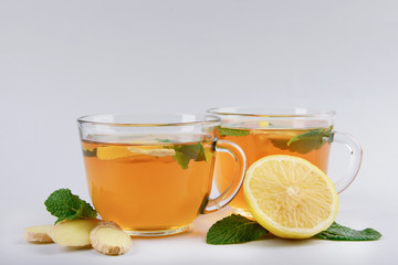 Cups of delicious tea with mint, ginger and lemon on grey background