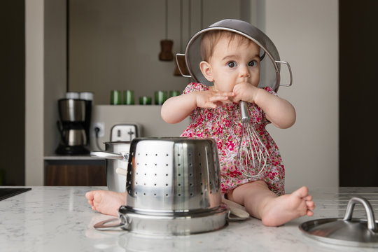 Cute baby sitting on kitchen counter with colander on head playing with kitchenware
