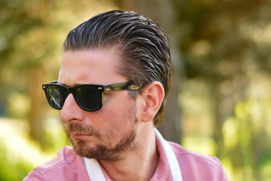 Young man's outdoors portrait looking at the camera who has sunglasses with natural green background. Neutral, happy, sad, disgust, fear, surprise Facial Emotion.