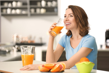 Beautiful woman drinking citrus juice in kitchen - obrazy, fototapety, plakaty
