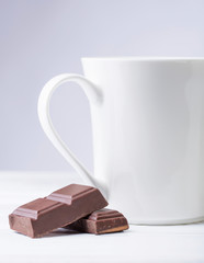 White mug of hot drink and bitter chocolate pieces.