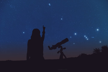 Silhouette of a girl and telescope with Milky Way stars.