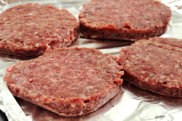 Raw beef burgers on a foil covered baking tray ready to be cooked
