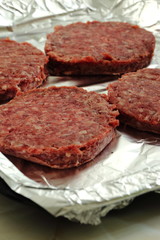 Raw beef burgers on a foil covered baking tray ready to be cooked