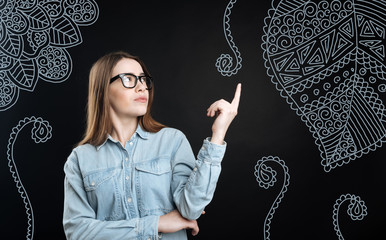 Unusual pattern. Young serious girl with poor eyesight pointing her finger to the ornament on the wall of her room and looking attentively at it