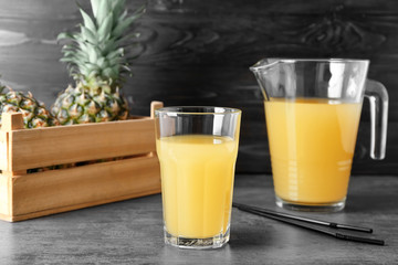 Glass and jug of tasty fresh pineapple juice on table