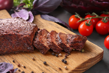 Cutting board with juicy meat and tomatoes on kitchen table