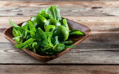 Fresh mint leaves and green limes in a wooden dish on a wooden background.