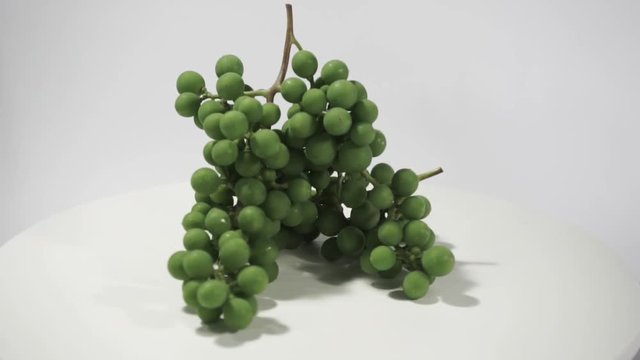 Green seedless grapes on a white table, rotation 360 degrees. White background.