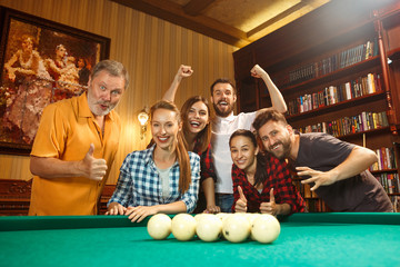 Young men and women playing billiards at office after work.