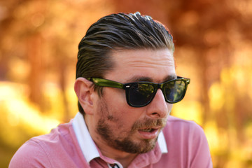 Young man's outdoors portrait looking at the camera who has sunglasses with natural green background. Neutral, happy, sad, disgust, fear, surprise Facial Emotion.