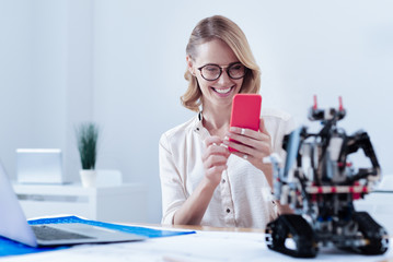 Modern development. Happy nice attractive woman smiling and looking at the robot while taking a photo of it