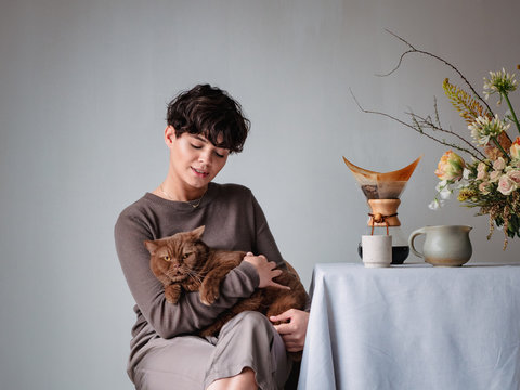 Young woman sitting with british shorthair cat against gray wall
