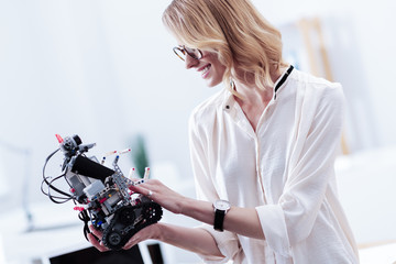 Mechanical robot. Joyful positive nice woman looking at her invention and smiling while being proud of it