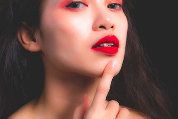 Charming beautiful woman is touching her chin. Attractive girl point and show her beautiful red lips. Glamour asian lady looks so beautiful. Glamour female has charming sexy face with black background