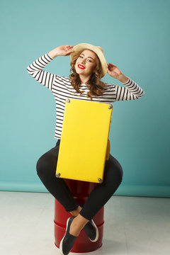 Young happy beautiful woman in hat holding yellow suitcase over blue background