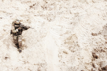 Special operations forces soldier, US army infantryman carefully sneaking, walking with service rifle in hands in hot sandy and rocky area. Military mission on Meddle East, modern warfare in desert