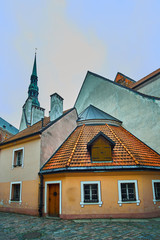 Fototapeta na wymiar Old medieval evening narrow street with Saint Peters Lutheran church on the background in Riga, Latvia. Retro styled.